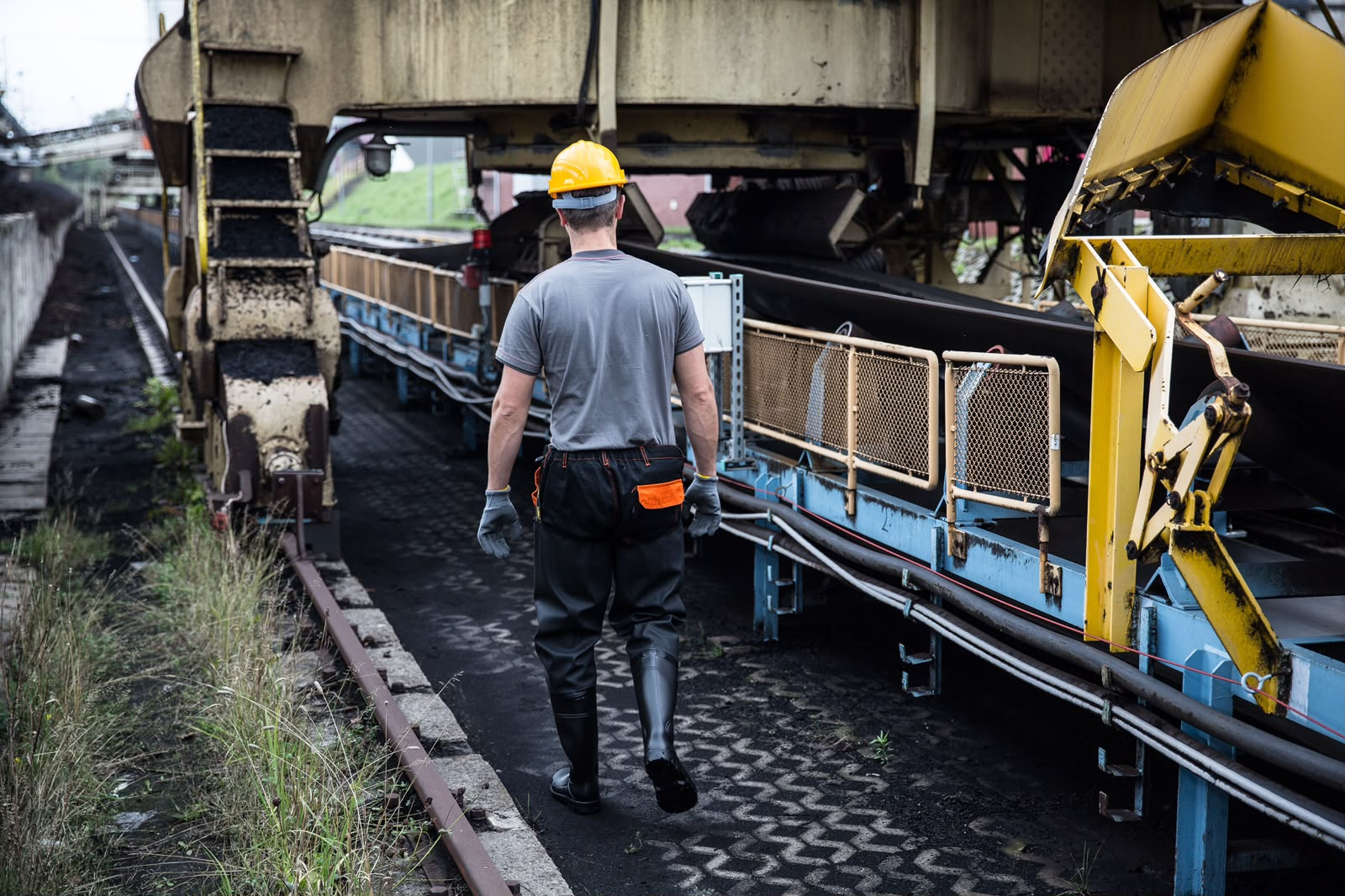 Operador inspecionando correia transportadora em pátio industrial